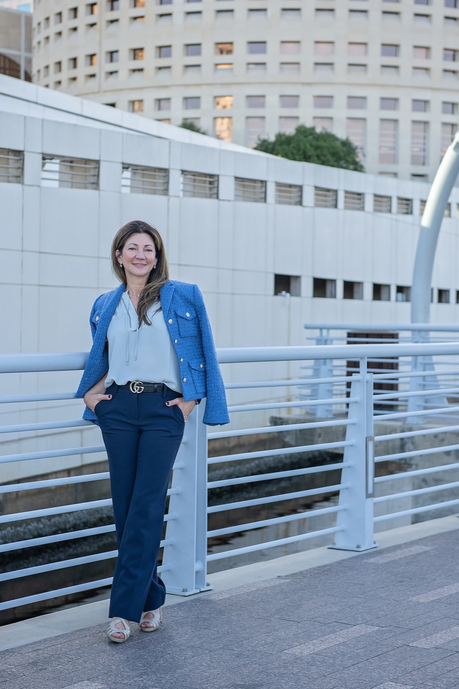 Carrie standing by the riverwalk railing in a blue jacket, smiling