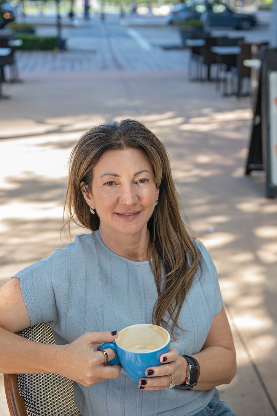 Carrie smiling at an outdoor cafe, holding a blue coffee cup