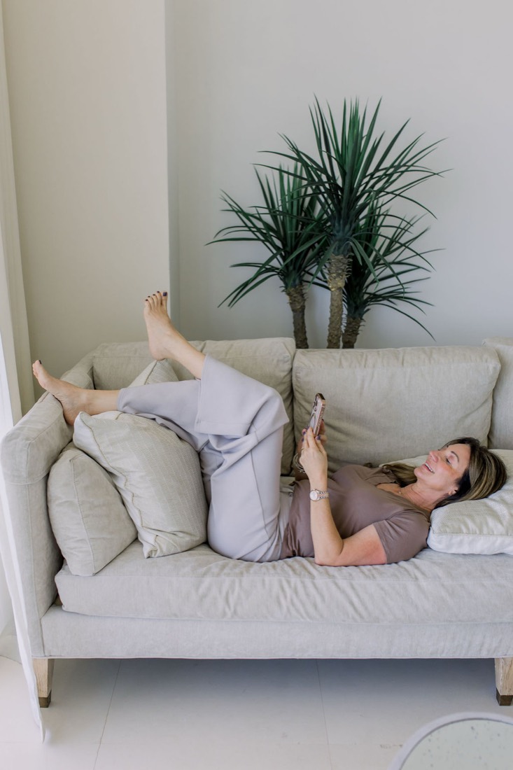 Carrie lying back on a white sofa with her feet up, looking at her phone