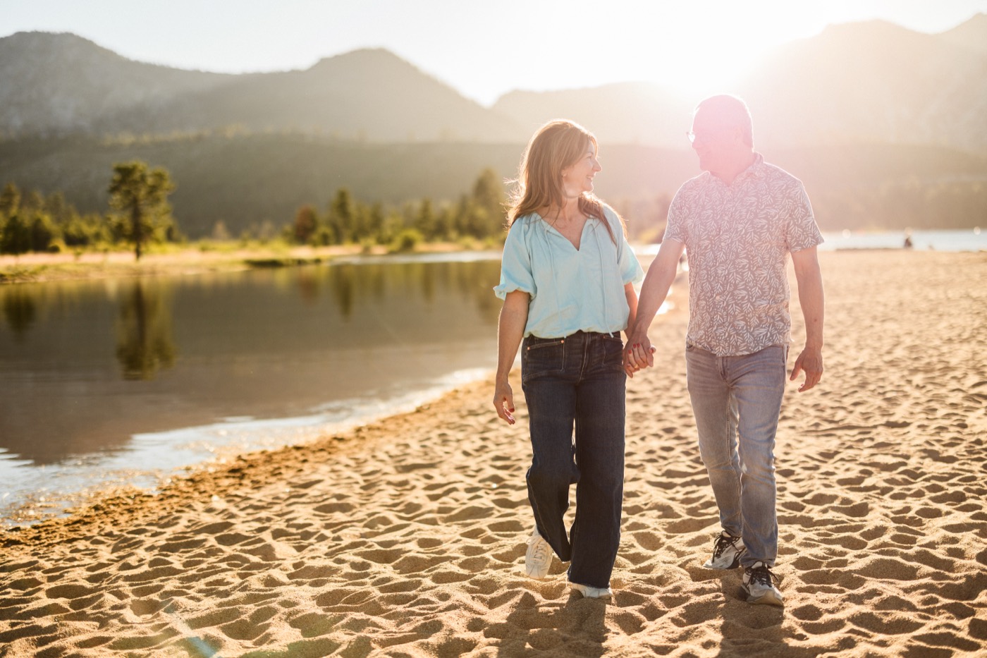 Carrie and her husband walking hand in hand on a lake beach